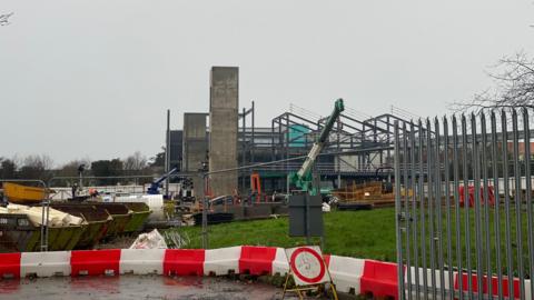 Les Ozouets College site - a building site with a crane behind a fence and a framework of a building.