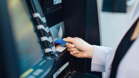 A stock image of a person putting a cash card into an ATM.