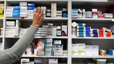 A pharmacist stocking shelves with piles of tablets at a chemist.