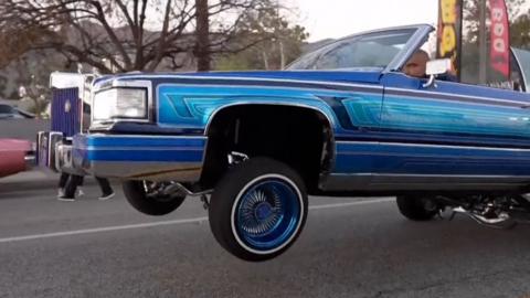 A blue lowrider with front wheels lifted above the ground.