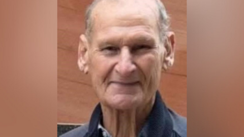 An older man is smiling as he looks at the camera.