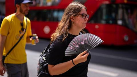 A woman using a fan to cool herself as she walks through central London