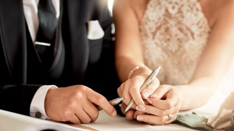 Couple sign wedding certificate, marriage registration and document paper for legal union. Closeup bride, groom and hands writing contract for celebration of love, commitment and agreement together