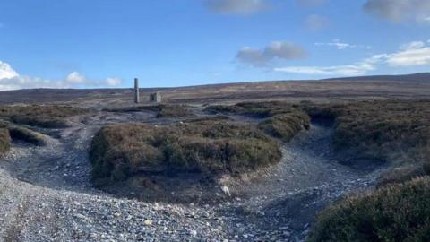 The site of an old mine. It has gravel tracks cut through heathland with mining towers in the distance.