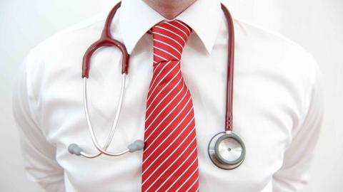 Close up image of a doctor in a white shirt and red striped tie posing with a stethoscope around his neck