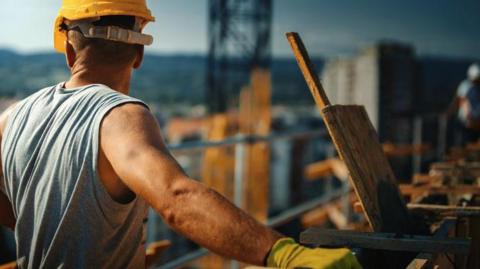 A closeup picture of a construction worker on top of a building in the sunshine, taking a short break.