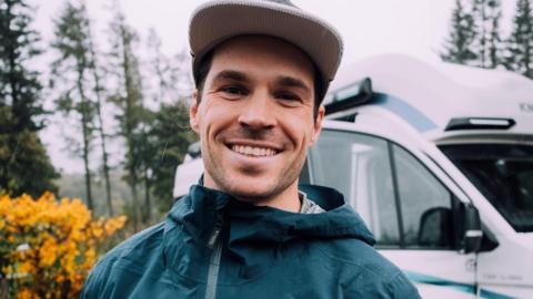 James Norbury. He is wearing a grey hat and a green waterproof jacket. He is smiling at the camera. 