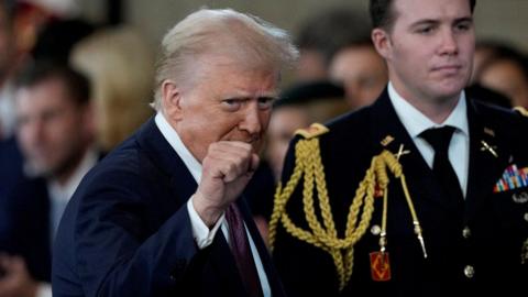 Donald Trump gestures with a clenched fist, in front of a member of the US military, during the inauguration ceremony.