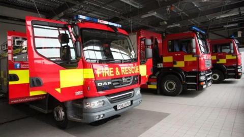 Three Lancashire Fire and Rescue fire engines lined side by side at a station. One has the cab doors open.