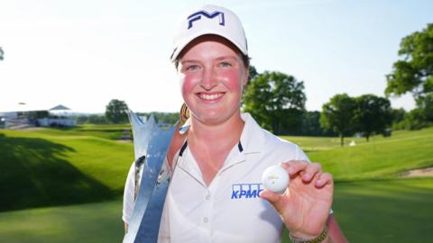Lottie Woad smiling and holding a trophy and a golf ball