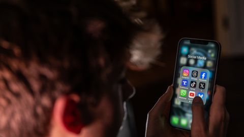 A teenage boy is pictured looking at his phone. On the screen there are a range of icons for social media sites, including Instagram, Threads, Facebook and TikTok. 
