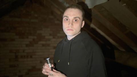 Joe Edgson is pictured inside a dark attic with a torch shining