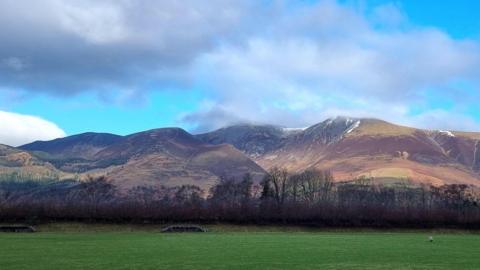 A green field with mountains behind and blue sky with some clouds