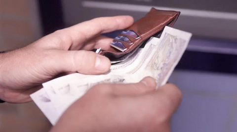 A close-up of hands putting banknotes into a leather wallet