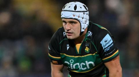 Curtis Langdon, wearing a white scrum cap, is leaning forward as if preparing to make a tackle.