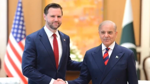 JD Vance and Pakistani PM Vance wearing suits, shaking hands and looking at the camera.