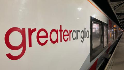 Side view of a Greater Anglia train with carriages running the length of the platform at a station
