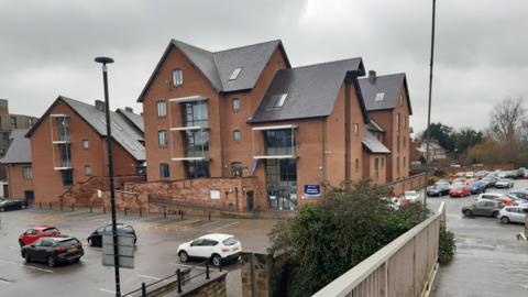 A large brick building with lots of windows and a car park surrounding it.