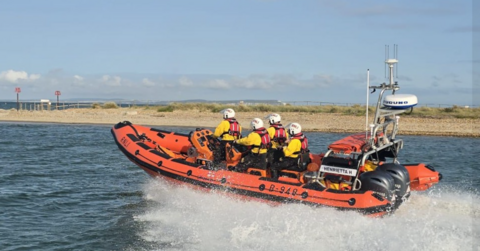 Mudeford RNLI lifeboat and four crew in yellow jackets with red buoyancy aids.