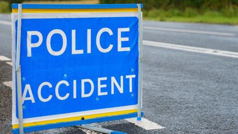 A police accident sign on a road, with 'police accident' in bold white letters on a blue background.