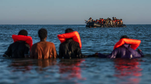 Asylum seekers wearing life vests are seen floating in the ocean as another small boat approaches in the background