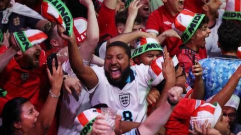 A man in an England shirt in the middle of a crowd of people celebrating