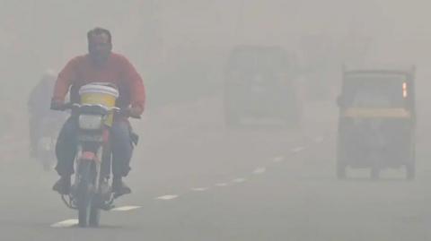 A man on a motorbike driving through a fog filled city