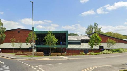 Farnham leisure centre. It is a brown building by a roadside, the sky is blue