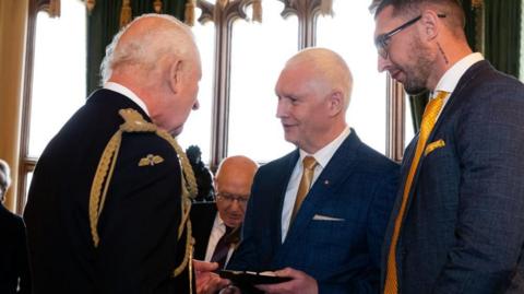 Bryn Hughes receives the Elizabeth Emblem from King Charles 