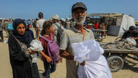 Palestinian man and woman carry bags of aid. They look visibly upset. 