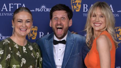 Philippa Dunne and Lucy Punch smiling either side of Laurence Rickard, with his mouth open in exclamation
