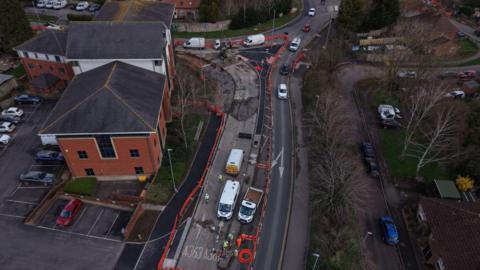 An aerial view of cars, white vans, a red building.