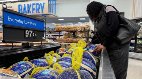 A person looks at frozen turkeys in a grocery store aisle, in front of a sign reading "Everyday Low Price".