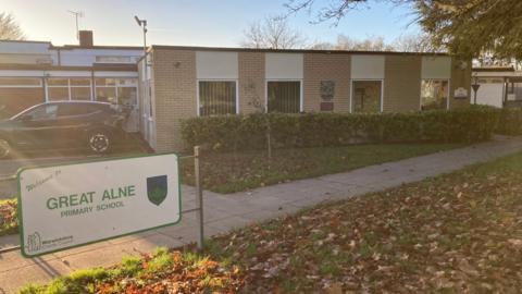 There is a sign saying welcome to Great Alne Primary school in front of the school building.