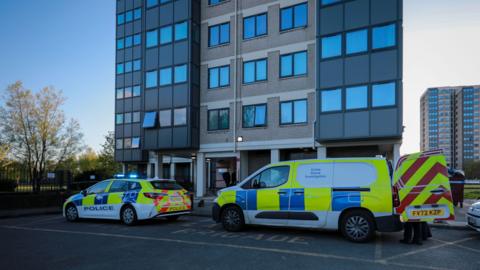 Police car and crime scene investigation van at bottom of tower block