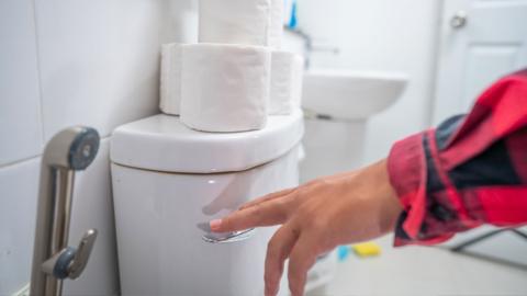 A hand operates a toilet flush in a bathroom