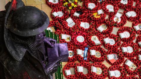 Poppy wreaths laid below a statue of a man reading