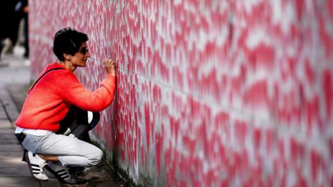 Members of the public observe the National Covid Memorial Wall, a public mural painted by volunteers to commemorate the victims of the COVID-19 pandemic in the United Kingdom, opposite the Houses of Parliament in Londo