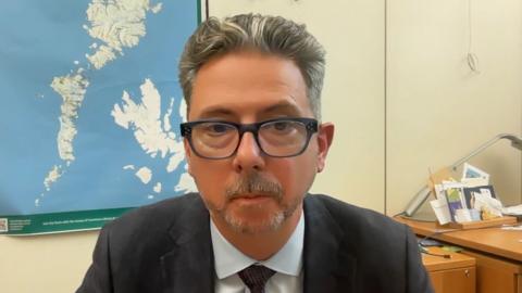 Torcuil Crichton, BP nan Eilean Siar, na shuidhe air beulaibh chamera.