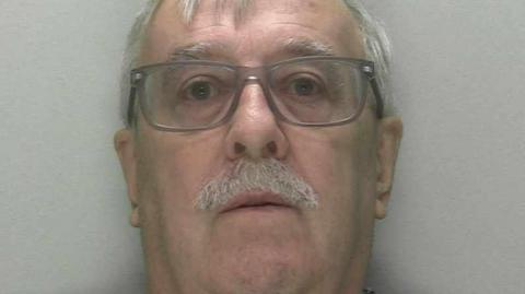 A man with a moustache and wearing glasses is pictured
