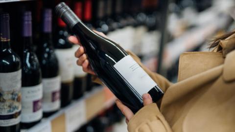 Person lifting wine bottle off shelf