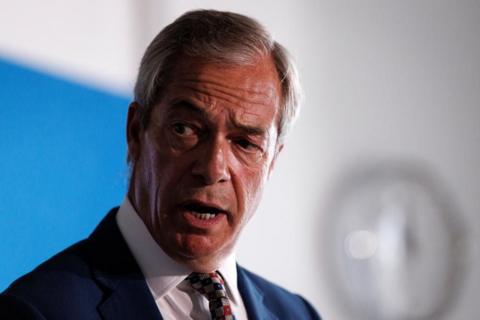 Headshot of Nigel Farage speaking a news conference. He is wearing a dark suit and multi-coloured tie.