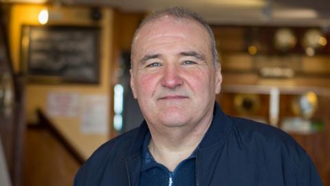 Lee Castleton, who is smiling slightly and wearing a navy jacket over a navy casual polo shirt