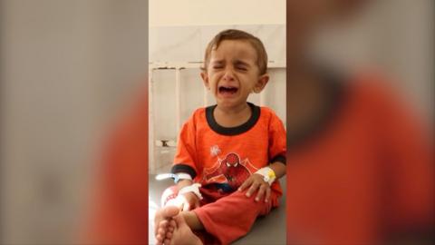 A toddler in orange Spider-Man pyjamas sits on a bed crying