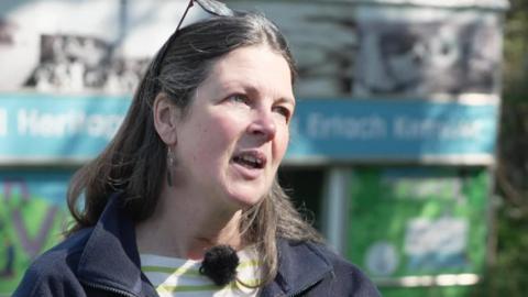 Trust education and outreach manager Caroline Davey. She is wearing a blue coat and a green and white striped T-shirt. She had long brown hair and glasses on her head. 