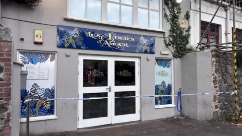 The outside of Les Folies d'Amour night club. The doors are closed and there is police tape across the front 
