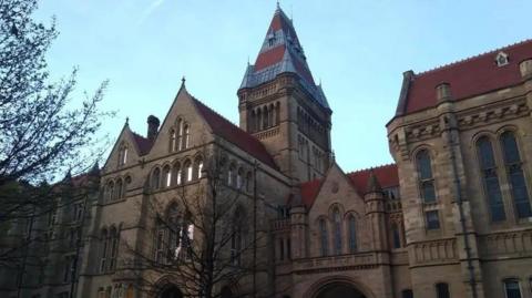 The spires of a stone university building loom towards the sky on a clear day.