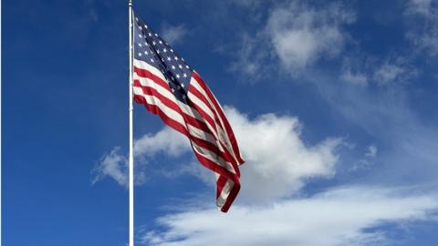 American flag blowing in the wind with a partly cloudy blue sky, USA
