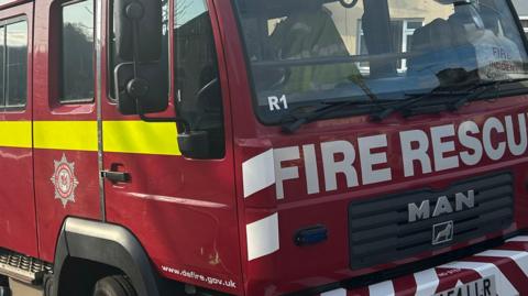 A generic shot of the front of a fire truck from Devon and Somerset Fire and Rescue Service. It is red with fire rescue across the front, a bright yellow stripe down the side and the logo