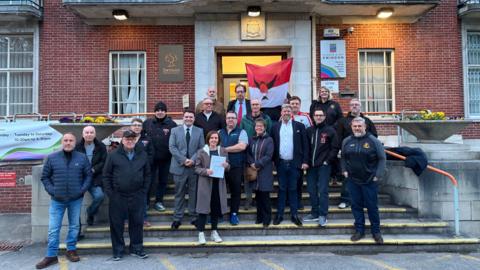 A group of people outside a council building looking at the camera and smiling